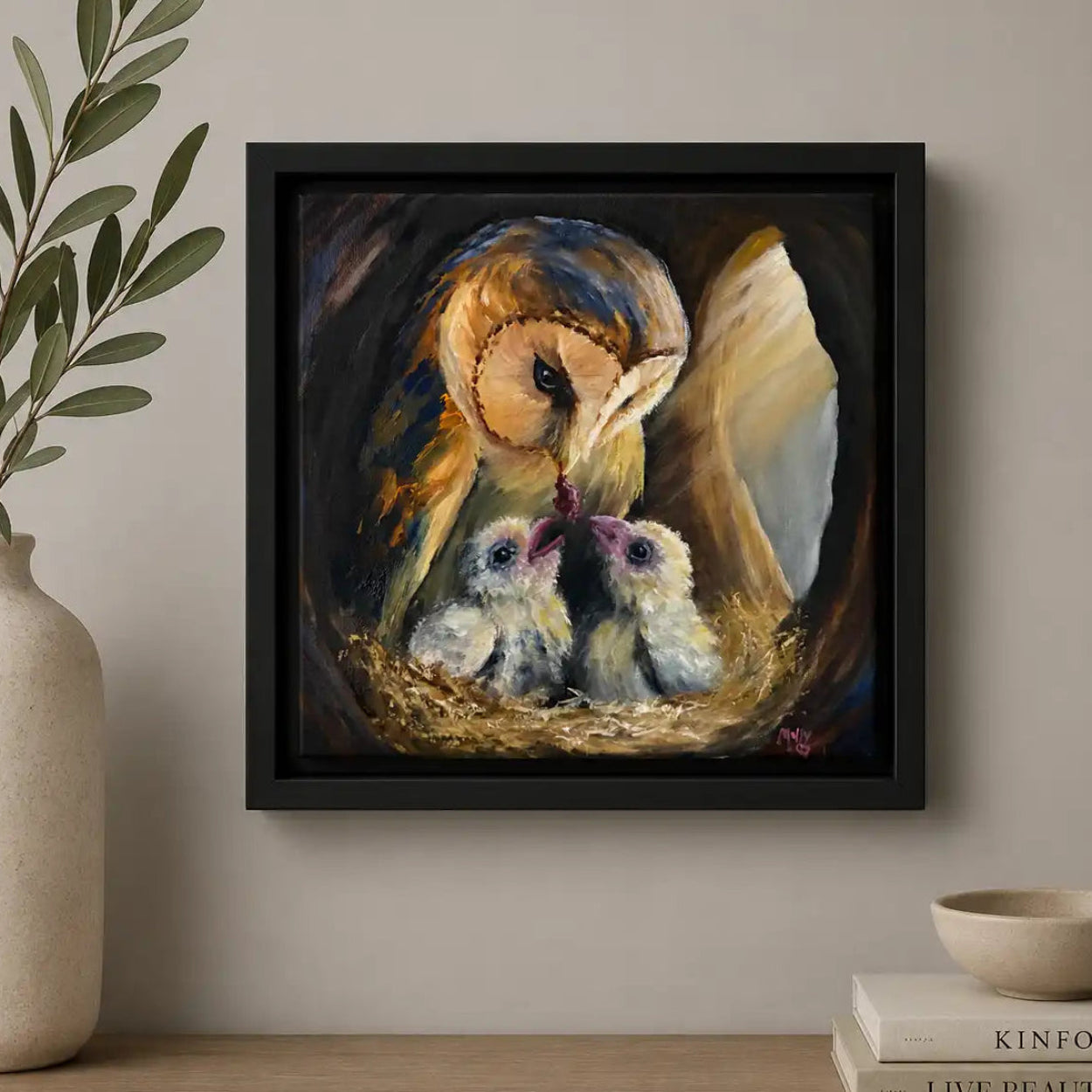 Framed artwork of an owl and chicks on a wall above a wooden shelf with decor items.