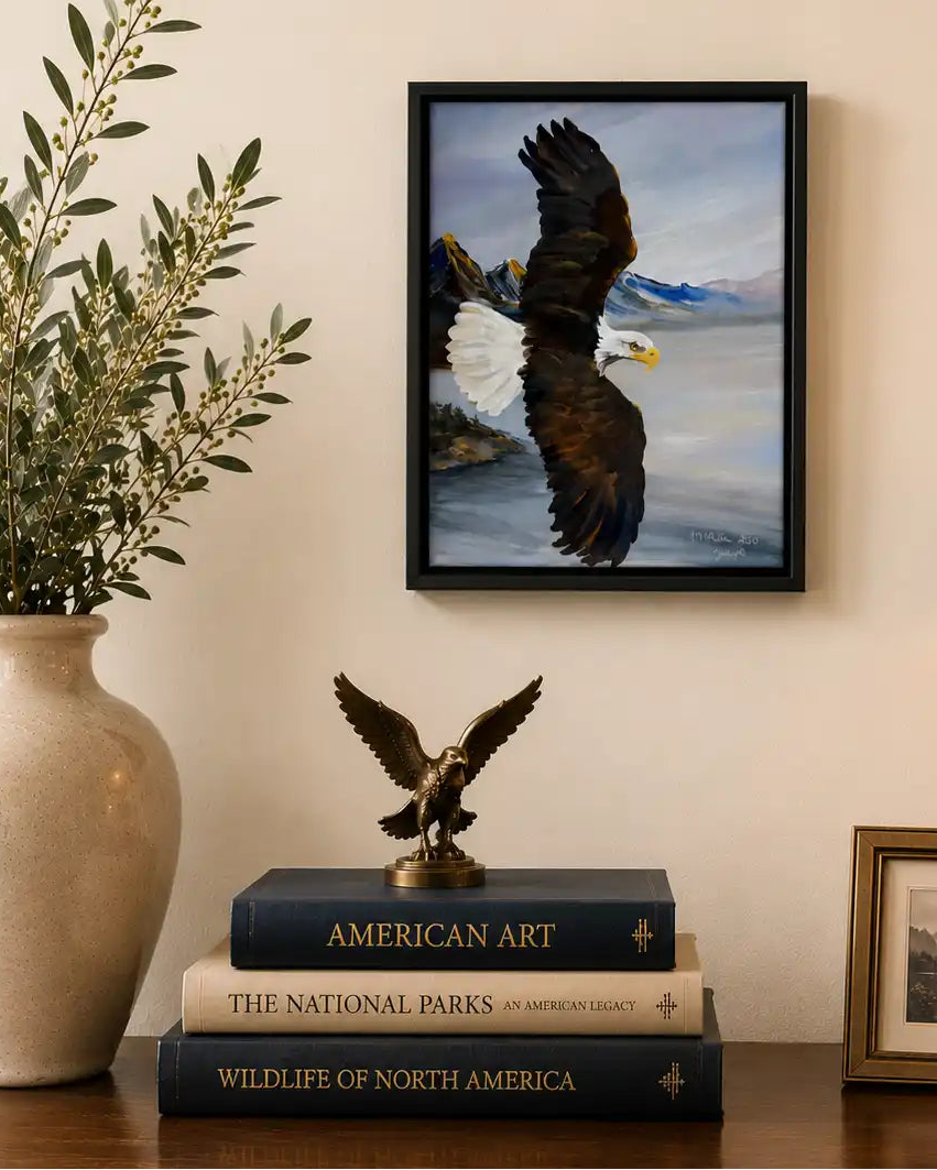 Framed picture of a bald eagle on a wall above books with decorative items on a table. Molly's Fine Art